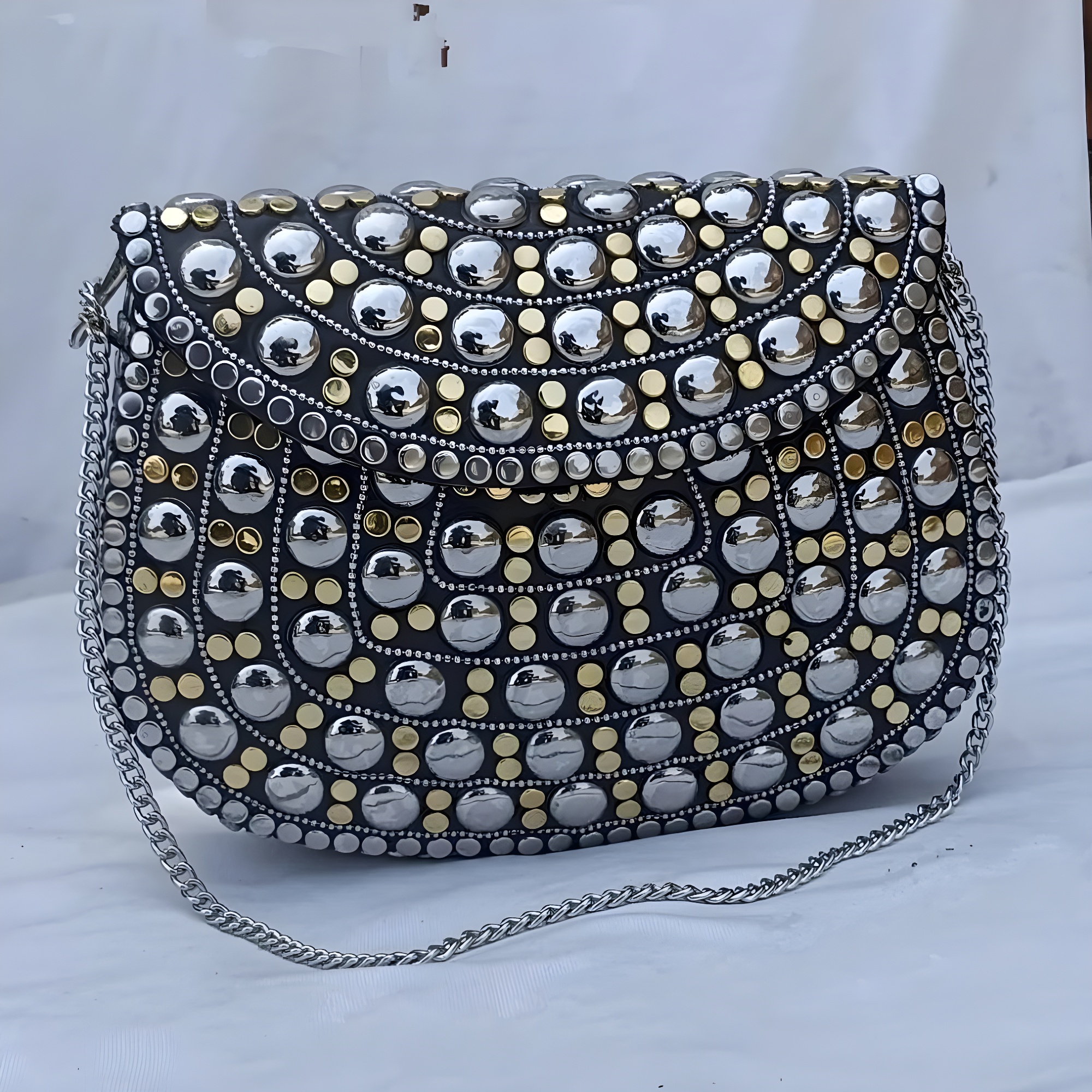Black handbag adorned with silver and gold studs, featuring a chain strap.